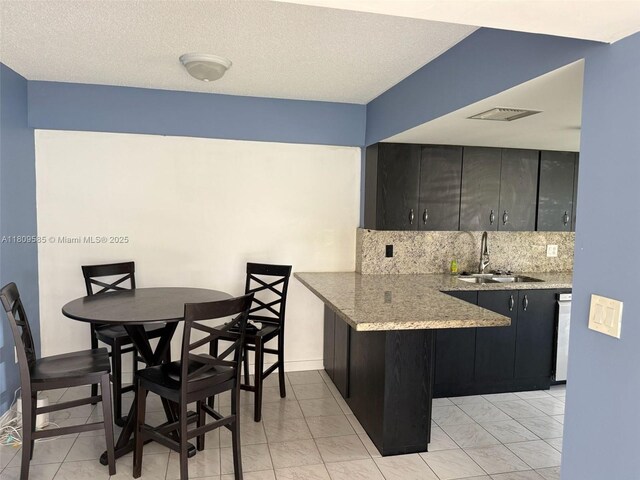 4168 Inverrary Dr Unit 111, Lauderhill, FL 33319 - kitchen featuring decorative backsplash, light stone counters, a textured ceiling, a peninsula, and dark cabinetry