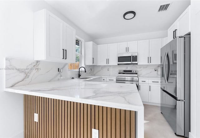 1470 SE 26th Ave, Homestead, FL 33035 - kitchen with appliances with stainless steel finishes, a peninsula, decorative backsplash, light stone counters, and white cabinetry
