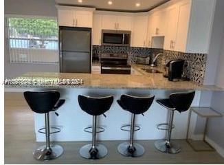 220 Kings Point Dr Unit 106, Sunny Isles Beach, FL 33160 - kitchen featuring stainless steel microwave, electric range, freestanding refrigerator, a peninsula, and tasteful backsplash