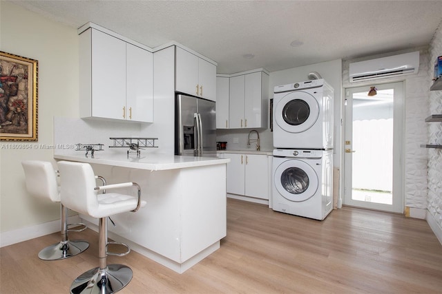 5920 SW 94th Ave, Miami, FL 33173 - laundry area featuring stacked washer and clothes dryer, a wall unit AC, light wood finished floors, baseboards, and a textured ceiling