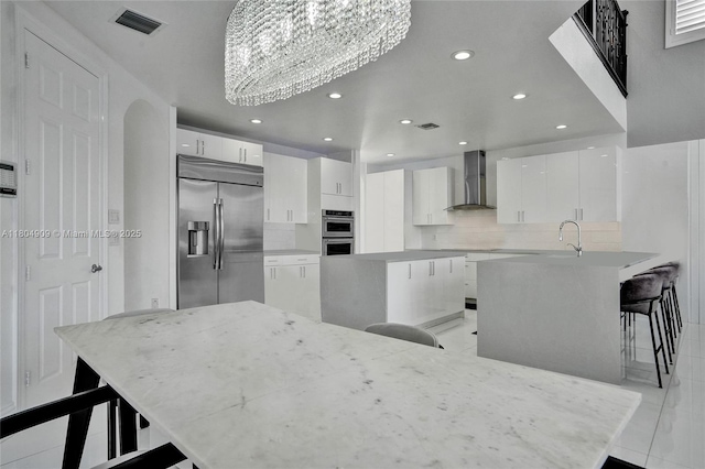 10457 Laurel Rd, Davie, FL 33328 - kitchen featuring appliances with stainless steel finishes, wall chimney range hood, modern cabinets, a breakfast bar, and a chandelier