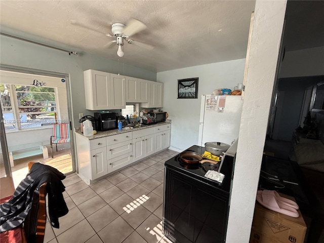 7951 NW 30th St, Davie, FL 33024 - kitchen with freestanding refrigerator, a ceiling fan, white cabinets, light tile patterned floors, and black microwave