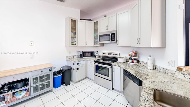 14723 SW 155th Pl, Miami, FL 33196 - kitchen with stainless steel appliances, light tile patterned floors, glass insert cabinets, light stone countertops, and white cabinetry