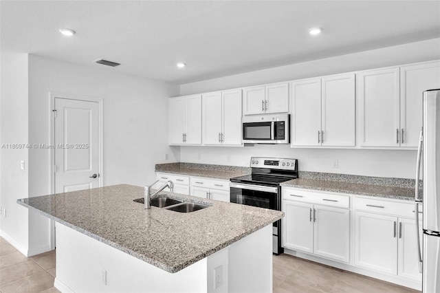 1130 SW Jericho Ave, Port St Lucie, FL 34953 - kitchen with appliances with stainless steel finishes, white cabinetry, light stone countertops, light tile patterned floors, and an island with sink