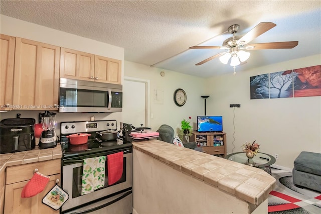 5156 NE 6th Ave Unit 227, Oakland Park, FL 33334 - kitchen featuring stainless steel appliances, tile counters, light brown cabinets, a peninsula, and a ceiling fan