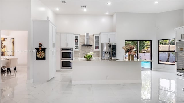 10412 NW 6th St, Coral Springs, FL 33071 - kitchen with appliances with stainless steel finishes, a towering ceiling, wall chimney exhaust hood, a kitchen island with sink, and light marble finish floors