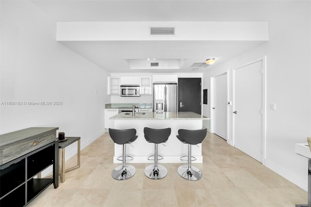 888 Biscayne Blvd Unit 3702, Miami, FL 33132 - kitchen featuring appliances with stainless steel finishes, a tray ceiling, a breakfast bar, white cabinetry, and light stone counters