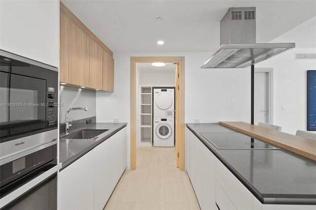 1000 Brickell Plz Unit 4209, Miami, FL 33131 - kitchen with stacked washing machine and dryer, exhaust hood, black electric stovetop, a sink, and stainless steel oven