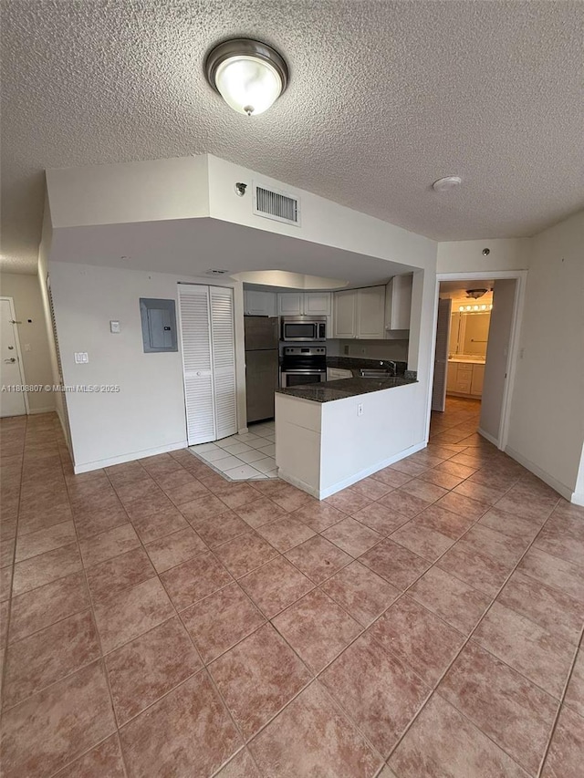 8911 Collins Ave Unit 1103, Surfside, FL 33154 - kitchen featuring stainless steel appliances, a peninsula, a textured ceiling, light tile patterned floors, and dark countertops