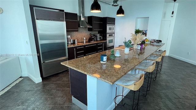 700 NE 25th St Unit 1703, Miami, FL 33137 - kitchen featuring built in appliances, wall chimney exhaust hood, a kitchen breakfast bar, dark cabinetry, and baseboards