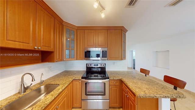 7 Montilla Ave, Coral Gables, FL 33134 - kitchen with stainless steel appliances, a peninsula, a kitchen bar, and brown cabinetry