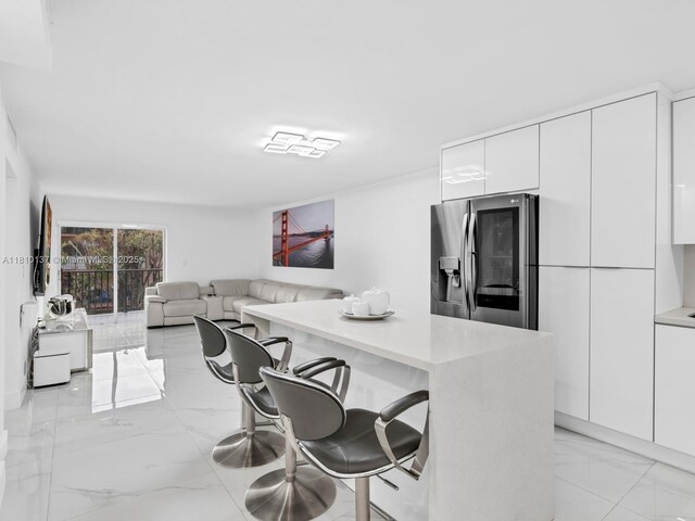 1890 W 56th St Unit 1307, Hialeah, FL 33012 - kitchen with stainless steel fridge with ice dispenser, modern cabinets, white cabinetry, a breakfast bar, and light marble finish flooring