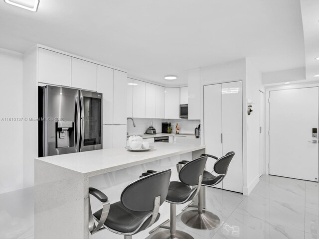 1890 W 56th St Unit 1307, Hialeah, FL 33012 - kitchen with stainless steel appliances, a breakfast bar, light countertops, light marble finish floors, and white cabinetry