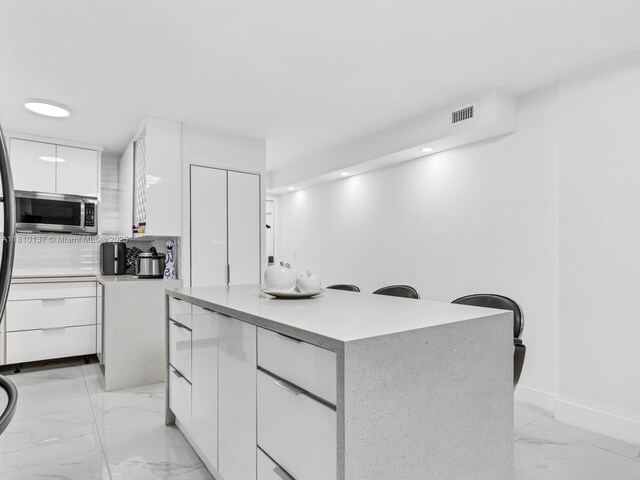 1890 W 56th St Unit 1307, Hialeah, FL 33012 - kitchen with stainless steel microwave, modern cabinets, white cabinetry, light marble finish flooring, and a kitchen island