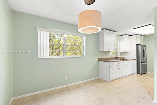 20 Lake Vista Trl Unit 107, Port St Lucie, FL 34952 - kitchen with freestanding refrigerator, a sink, a textured ceiling, baseboards, and white cabinetry