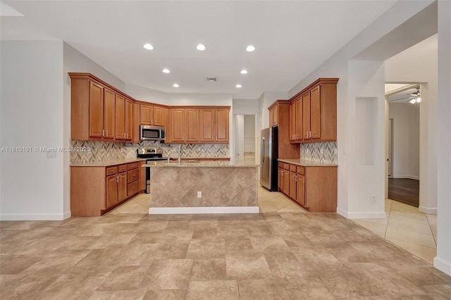 9212 Short Chip Cir, Port St Lucie, FL 34986 - kitchen featuring stainless steel appliances, recessed lighting, decorative backsplash, an island with sink, and brown cabinets