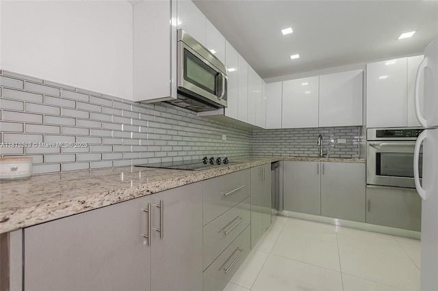 6039 Collins Ave Unit 307, Miami Beach, FL 33140 - kitchen featuring stainless steel appliances, light tile patterned flooring, modern cabinets, a sink, and white cabinetry