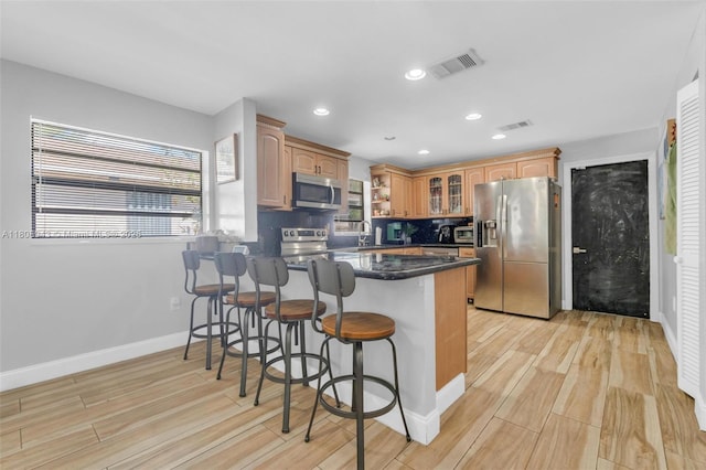 2412 Raleigh St, Hollywood, FL 33020 - kitchen with stainless steel appliances, a peninsula, glass insert cabinets, a breakfast bar area, and light wood-style flooring