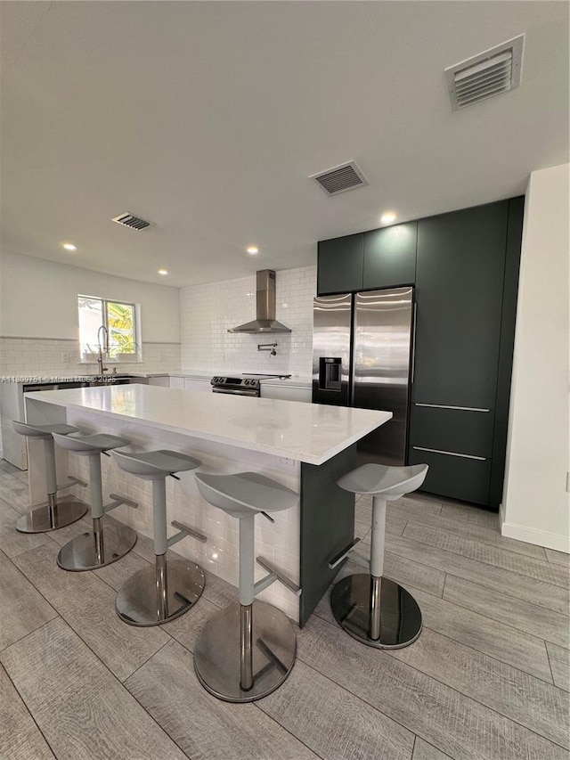 501 SW 18th St, Pompano Beach, FL 33060 - kitchen with wall chimney exhaust hood, light countertops, a breakfast bar area, stainless steel appliances, and light wood-style flooring