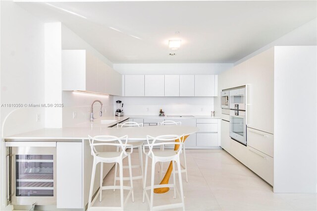 16901 Collins Ave Unit 2504, Sunny Isles Beach, FL 33160 - kitchen with oven, beverage cooler, a peninsula, a kitchen bar, and light countertops