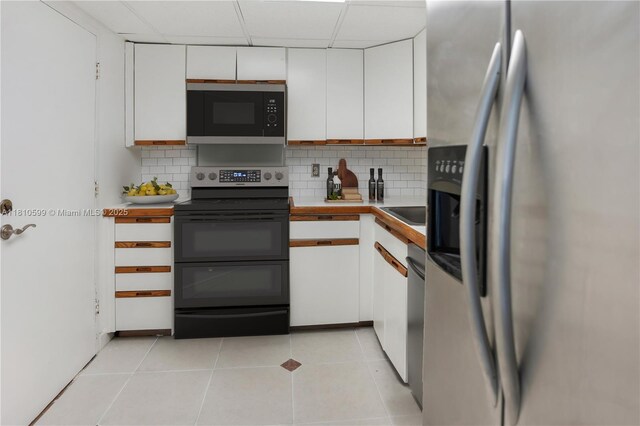 800 W Ave Unit 920, Miami Beach, FL 33139 - kitchen with black appliances, white cabinets, backsplash, and light tile patterned flooring