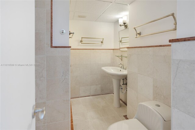 800 W Ave Unit 920, Miami Beach, FL 33139 - bathroom featuring tile walls, toilet, a paneled ceiling, a wainscoted wall, and a sink