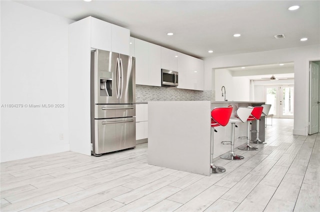 1328 NW 93rd Ter, Coral Springs, FL 33071 - kitchen with stainless steel appliances, light wood-style flooring, white cabinetry, ceiling fan, and a kitchen breakfast bar
