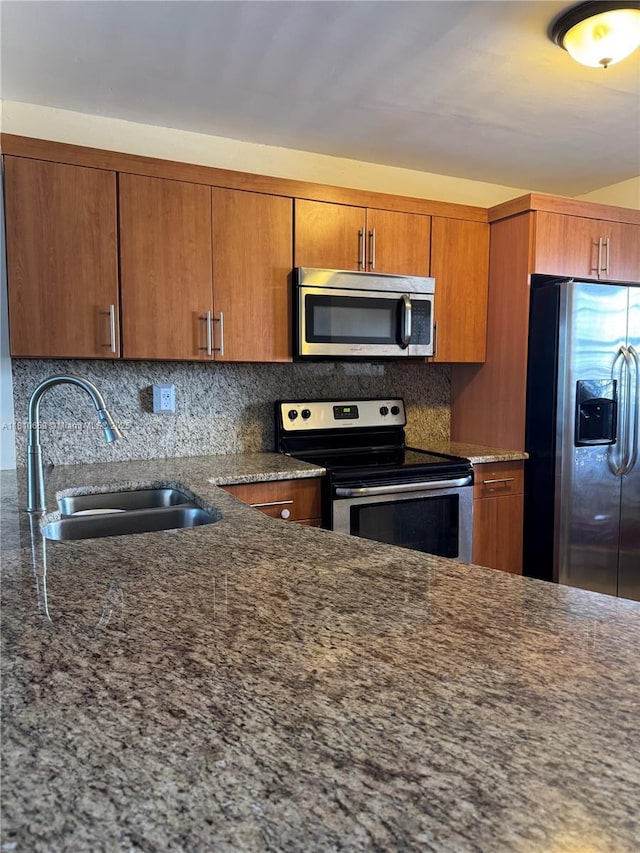 1780 NE 191st St Unit 412-2, Miami, FL 33179 - kitchen with appliances with stainless steel finishes, a sink, backsplash, brown cabinetry, and dark stone counters