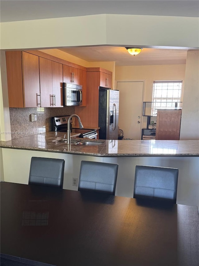 1780 NE 191st St Unit 412-2, Miami, FL 33179 - kitchen featuring appliances with stainless steel finishes, a sink, brown cabinets, tasteful backsplash, and dark stone counters