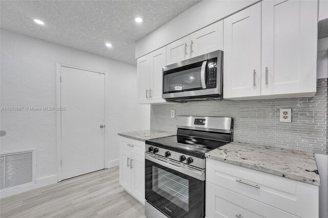 7204 NW 76th Dr, Tamarac, FL 33321 - kitchen with stainless steel appliances, decorative backsplash, light wood-style floors, light stone counters, and white cabinetry