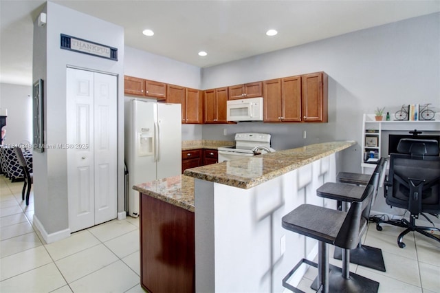 9051 SW 227th St Unit 2, Cutler Bay, FL 33190 - kitchen with white appliances, a peninsula, a breakfast bar, light stone countertops, and light tile patterned floors