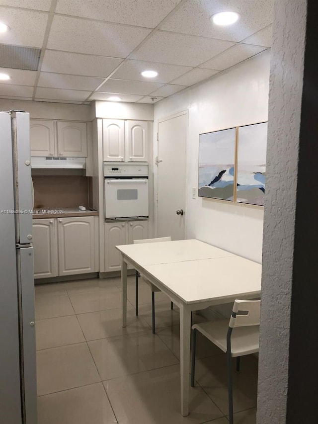 3901 S Ocean Dr Unit 1B, Hollywood, FL 33019 - kitchen featuring white appliances, under cabinet range hood, light tile patterned floors, a paneled ceiling, and white cabinetry