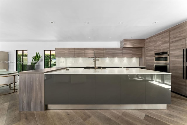 4250 Bay Point Rd, Miami, FL 33137 - kitchen with modern cabinets, a sink, stainless steel double oven, a large island with sink, and brown cabinetry