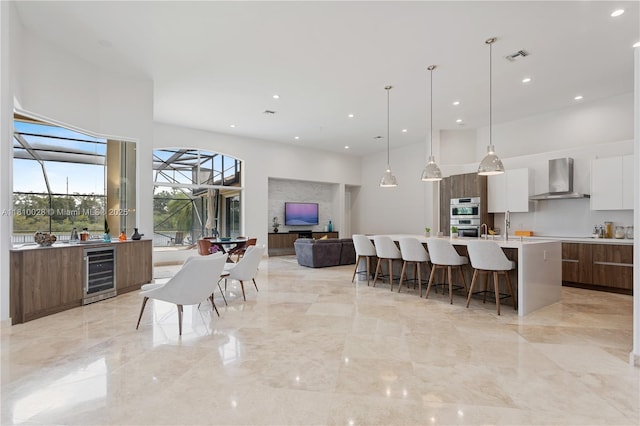 146 Dockside Cir, Weston, FL 33327 - kitchen featuring modern cabinets, wall chimney range hood, wine cooler, a kitchen breakfast bar, and a towering ceiling