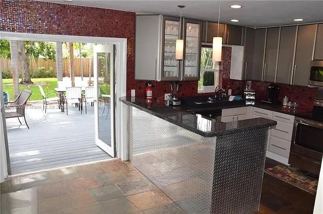 1215-1217 NE 16th Ave, Fort Lauderdale, FL 33304 - kitchen with dark countertops, appliances with stainless steel finishes, glass insert cabinets, a peninsula, and stone finish floors