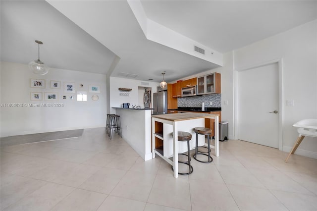 3131 NE 188th St Unit 2-506, Aventura, FL 33180 - kitchen featuring appliances with stainless steel finishes, a peninsula, backsplash, a kitchen bar, and brown cabinetry