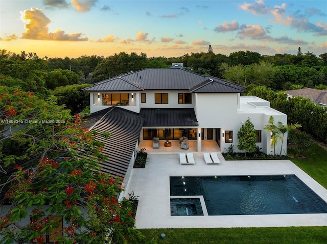 11001 SW 65th Ave, Pinecrest, FL 33156 - back of property at dusk featuring a standing seam roof, stucco siding, a patio, an outdoor pool, and a metal roof