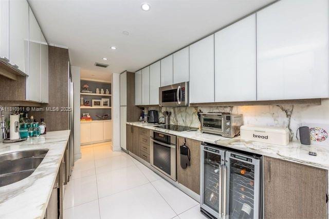 901 Brickell Key Blvd Unit 906, Miami, FL 33131 - kitchen with appliances with stainless steel finishes, light stone counters, backsplash, and wine cooler