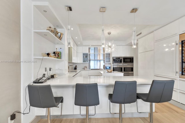 9701 Collins Ave Unit 2403S, Bal Harbour, FL 33154 - kitchen with black microwave, white cabinets, modern cabinets, light wood-style floors, and a breakfast bar