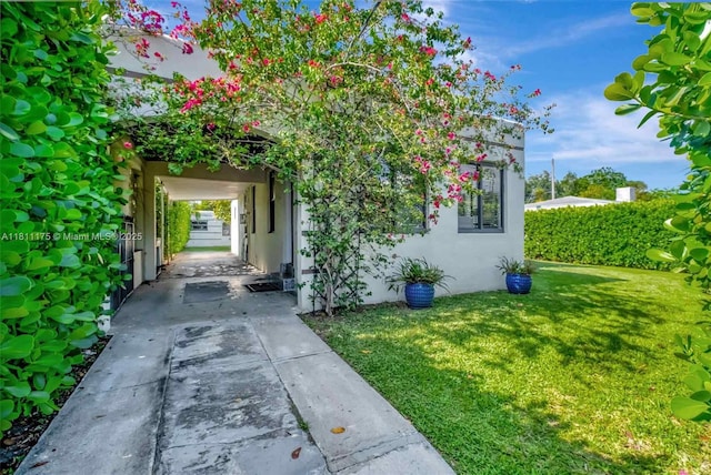 2763 NW 3rd St, Miami, FL 33125 - view of exterior entry featuring stucco siding, driveway, a yard, and a carport