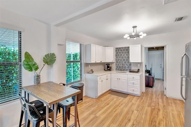 2763 NW 3rd St, Miami, FL 33125 - kitchen with freestanding refrigerator, backsplash, light countertops, white cabinetry, and a chandelier