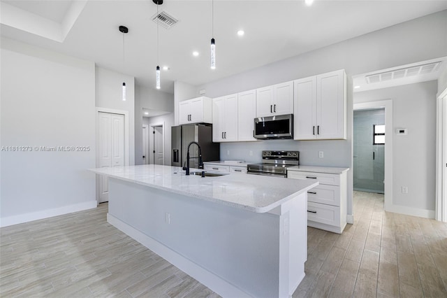 2709 58th St W, Lehigh Acres, FL 33971 - kitchen featuring stainless steel appliances, a sink, an island with sink, white cabinetry, and light wood-type flooring