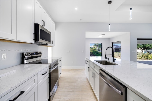 2709 58th St W, Lehigh Acres, FL 33971 - kitchen with stainless steel appliances, a sink, light wood-type flooring, hanging light fixtures, and white cabinets