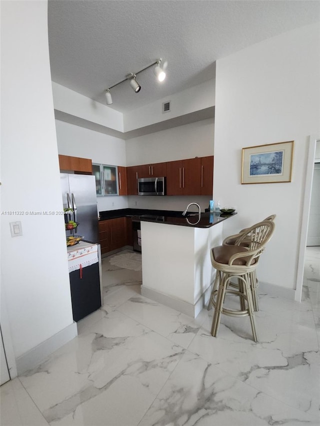 325 S Biscayne Blvd Unit 14, Miami, FL 33131 - kitchen with appliances with stainless steel finishes, a peninsula, dark countertops, light marble finish flooring, and a textured ceiling