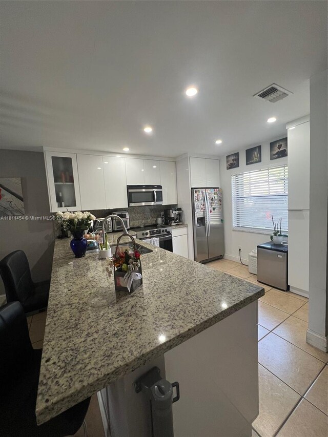 721 NW 105th Ter Unit 721, Pembroke Pines, FL 33026 - kitchen featuring appliances with stainless steel finishes, a peninsula, white cabinets, light stone counters, and light tile patterned flooring