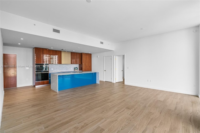 2678 Tigertail Ave Unit 513, Coconut Grove, FL 33133 - kitchen featuring light wood-style flooring, open floor plan, decorative backsplash, brown cabinetry, and a kitchen island