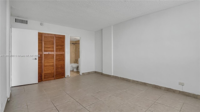 3660 NE 166th St Unit 603, North Miami Beach, FL 33160 - unfurnished bedroom featuring a textured ceiling, baseboards, a closet, connected bathroom, and light tile patterned floors