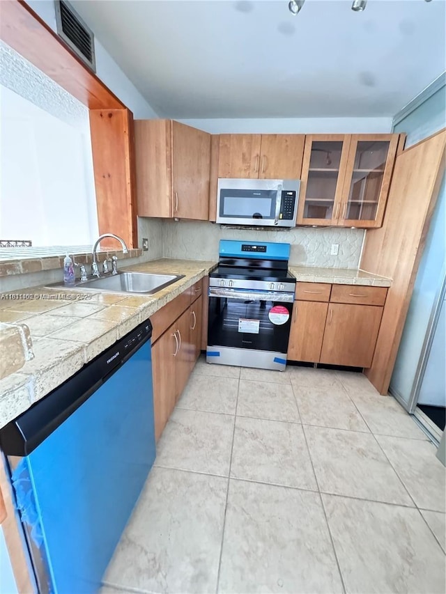 3660 NE 166th St Unit 603, North Miami Beach, FL 33160 - kitchen featuring appliances with stainless steel finishes, a sink, light countertops, glass insert cabinets, and brown cabinetry
