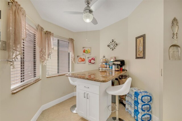 3831 NW 21st St, Coconut Creek, FL 33066 - kitchen with stone countertops, baseboards, white cabinets, a ceiling fan, and a breakfast bar