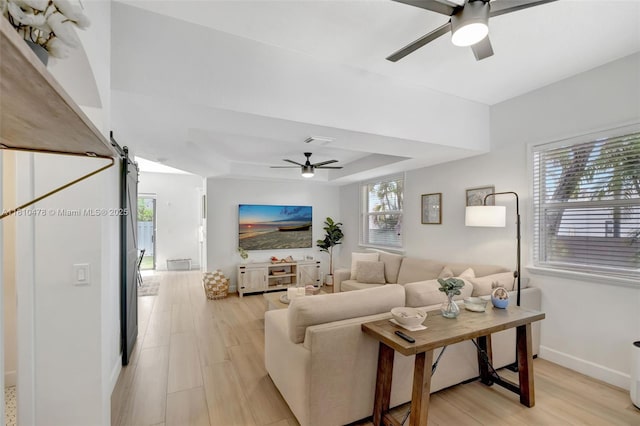 4413 NW 97th Pl, Doral, FL 33178 - living area with ceiling fan, a tray ceiling, a barn door, light wood-type flooring, and baseboards
